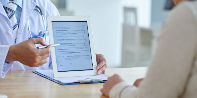 Close-up shot of physician pointing at screen of digital tablet, female patient listening to him with concentration